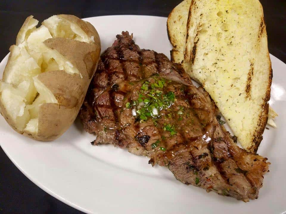 grilled ribeye with a slice of garlic bread and a baked potato on the side.